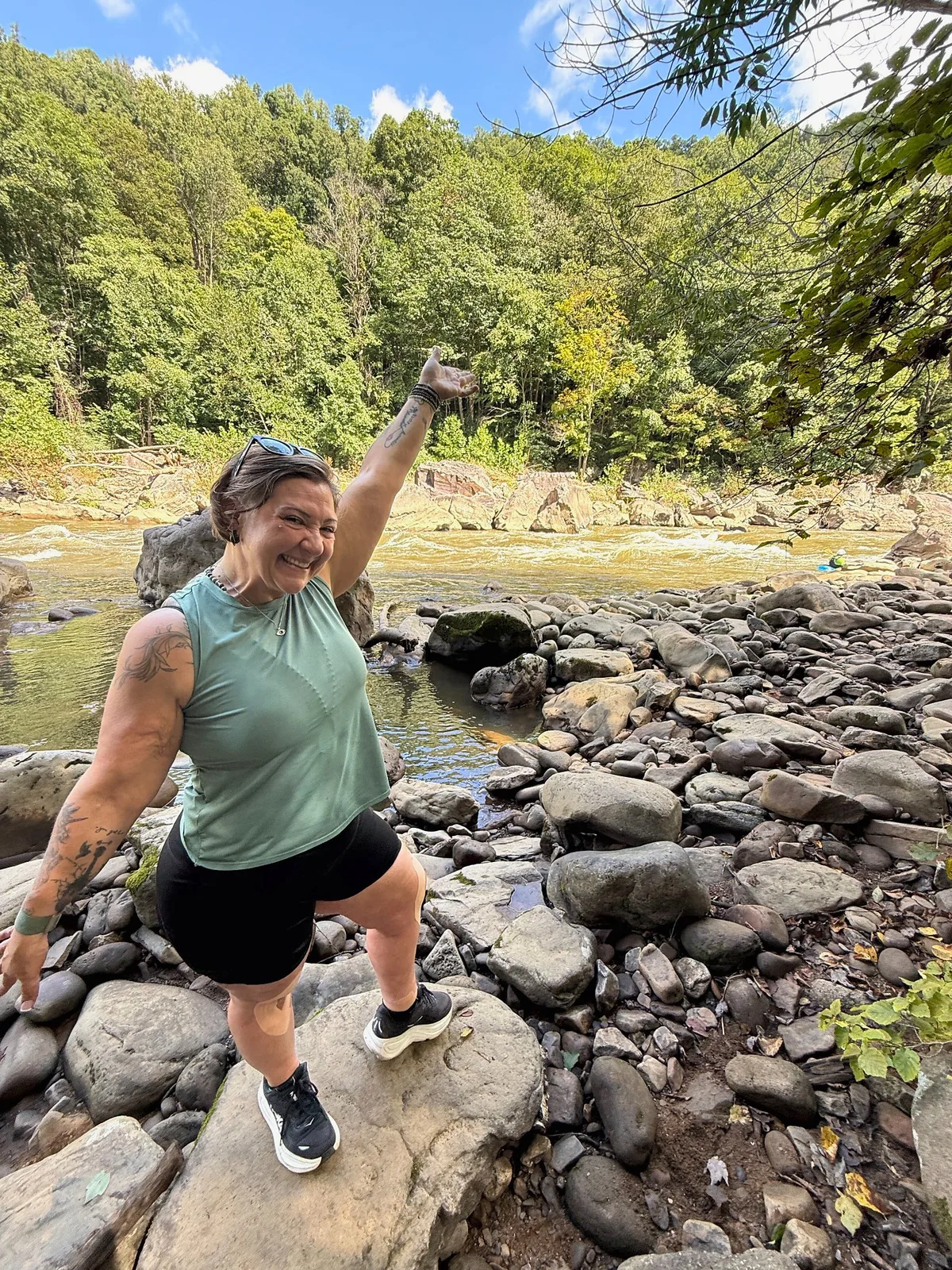 Desarae smiling beside a rocky river in the mountains