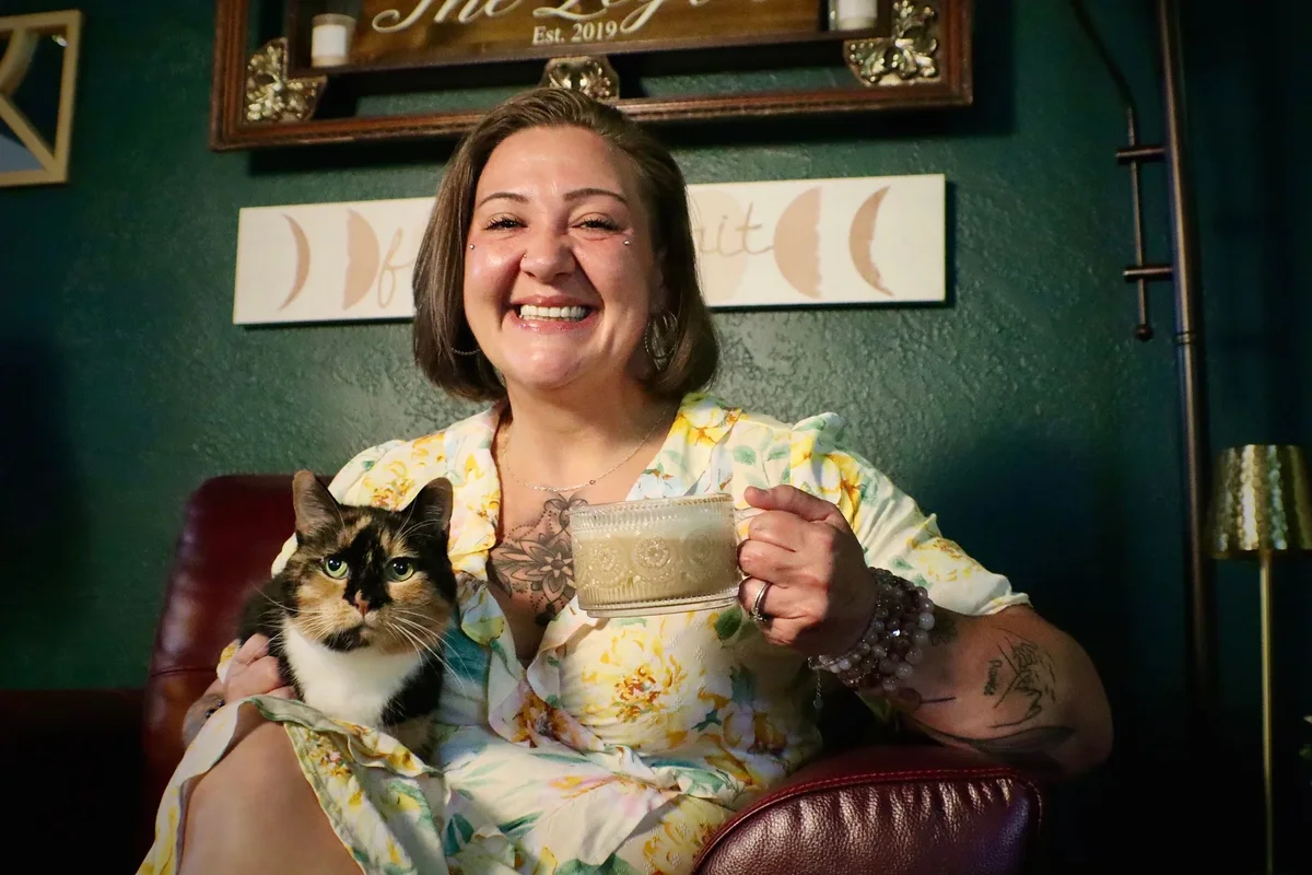 Desarae smiling with her cat and holding a coffee in her studio