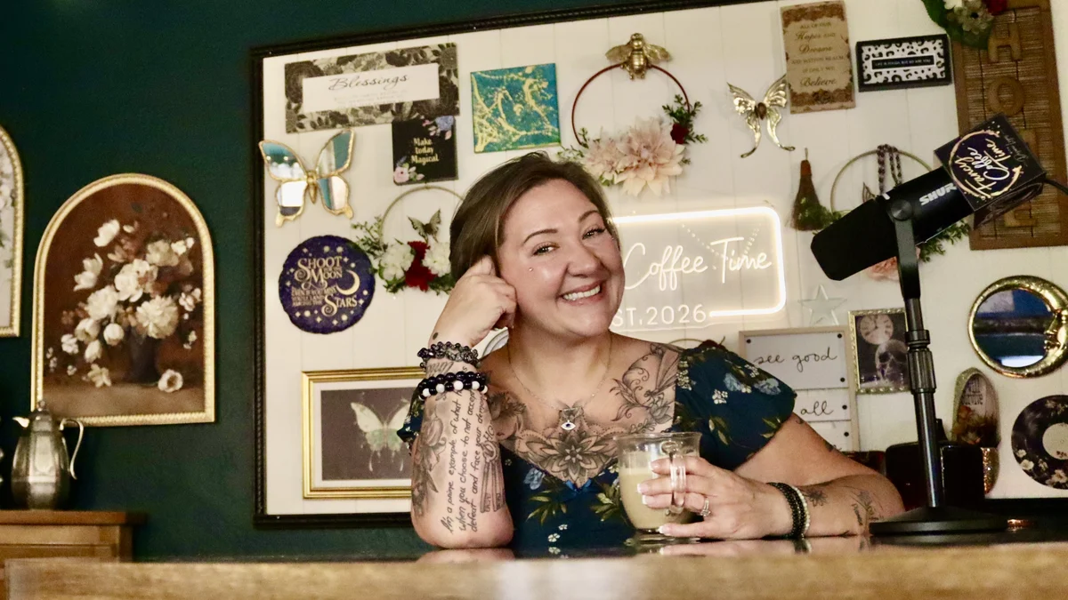 Desarae smiling in her studio with a coffee beside her microphone