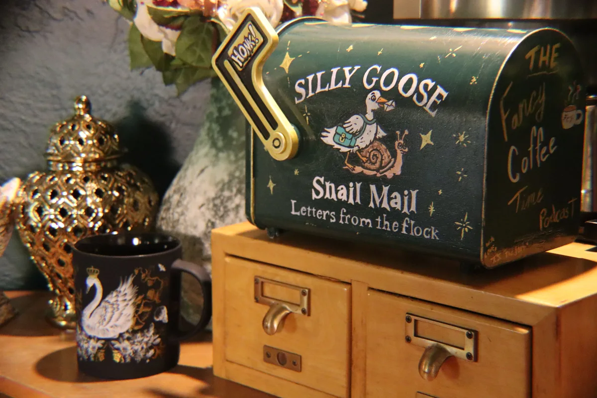 A hand-painted Silly Goose snail mail mailbox beside a patterned coffee mug